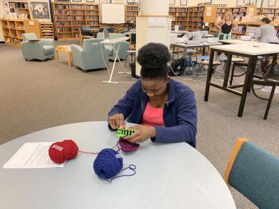 Student knitting for "Hats for Some"